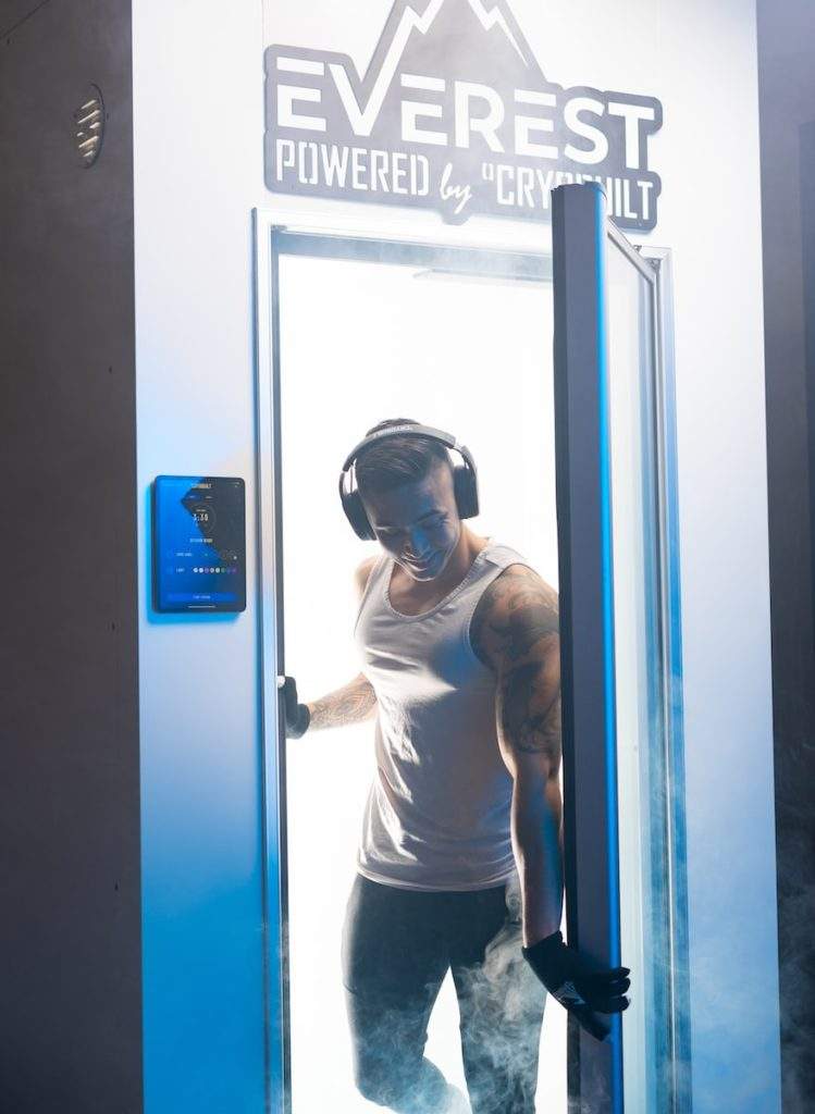 man in white long sleeve shirt wearing white goggles standing beside blue door