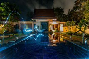 reflection of blue light crossing above pool near house during nighttime